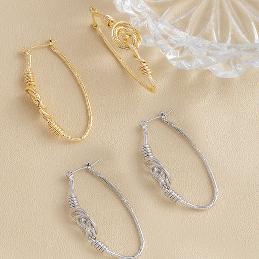 hoop earrings in gold and silver tones with textured and twisted details, arranged on a beige textured background with a clear glass dish in the corner.